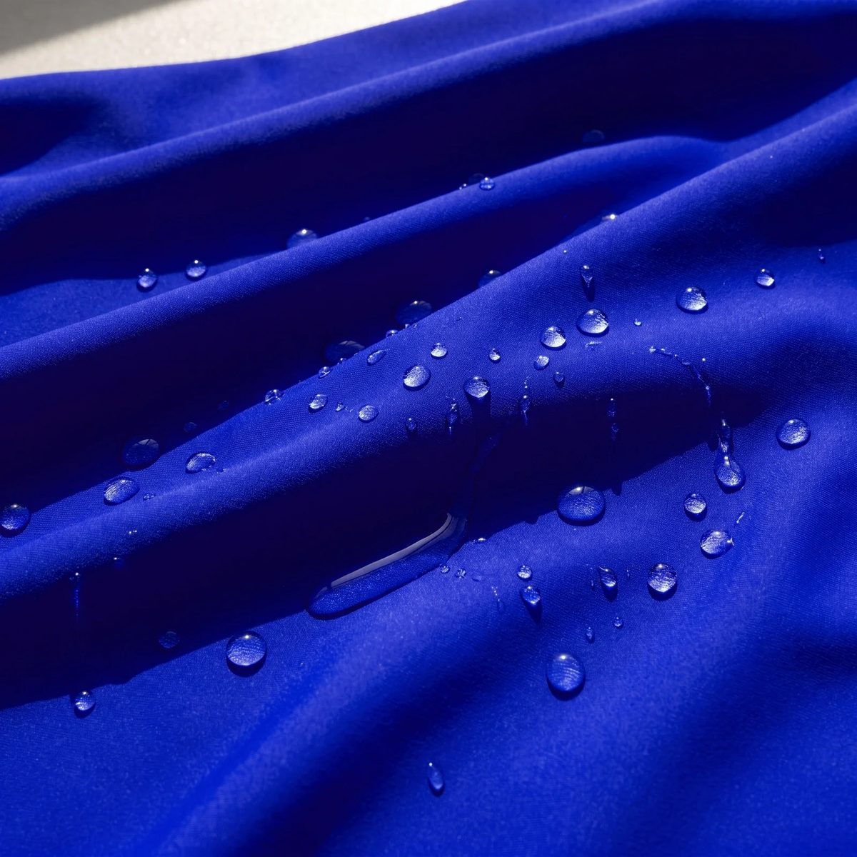 Gotas de agua perladas sobre la licra italiana UPF 50+ azul rey, que repele el agua