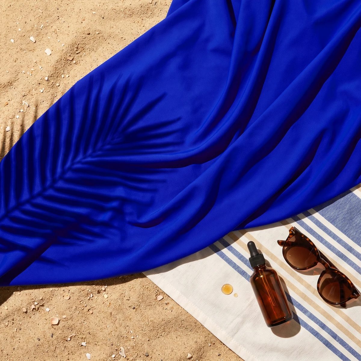 Licra italiana UPF 50+ azul rey al sol sobre una toalla, junto a un aceite bronceador