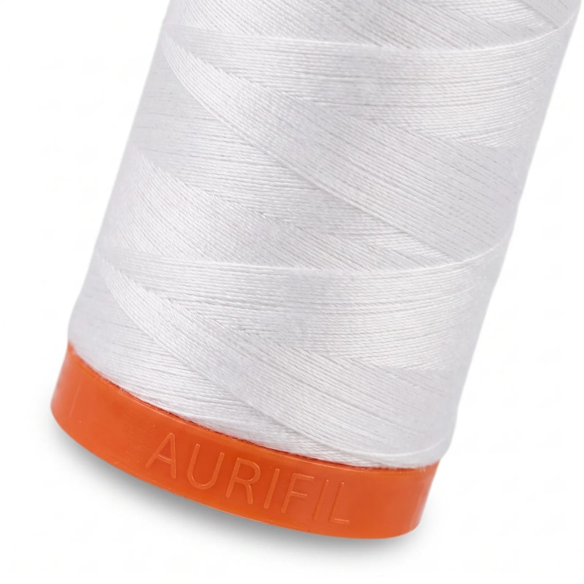 Macro del hilo Aurifil 50wt blanco enrollado en capas cruzadas sobre la base naranja del carrete