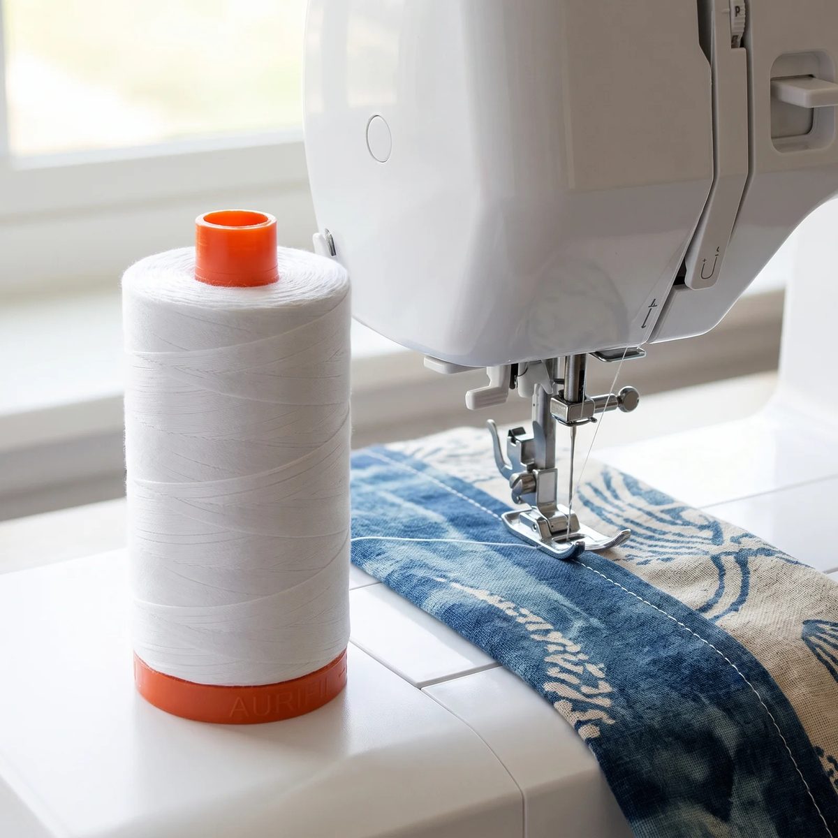 Carrete de hilo Aurifil 50wt blanco montado en una máquina de coser casera uniendo dos bloques de algodón