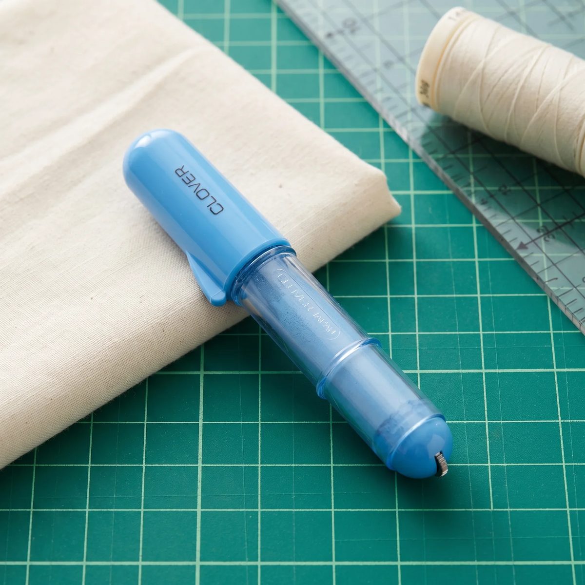 Tiza en lápiz Clover Chaco Liner sobre una mesa de corte junto a una tela de algodón crudo y una regla de modistería