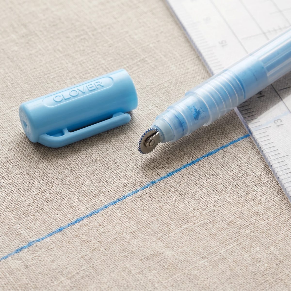 Línea fina de tiza azul trazada con la Clover Chaco Liner sobre lino crudo, siguiendo una regla