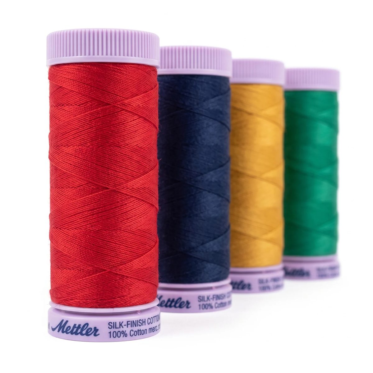 Cuatro carretes de hilo Mettler Silk-Finish de pie sobre fondo blanco, con el brillo mate del algodón mercerizado