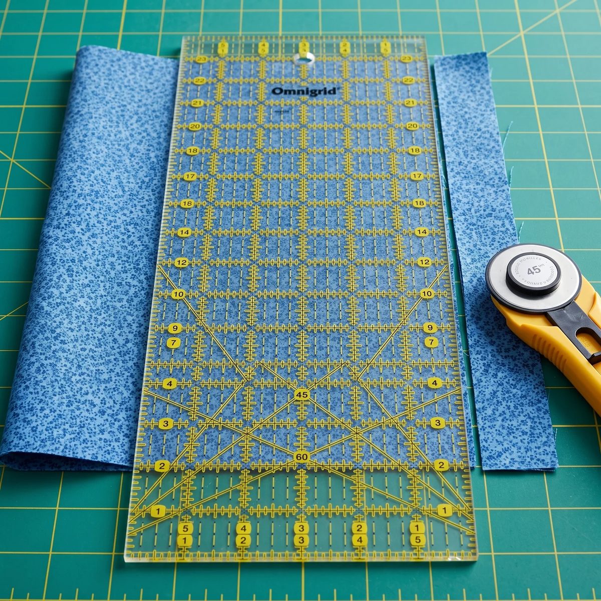 Regla Omnigrid 6 por 24 sobre tela de algodón doblada, con una tira recién cortada a lo largo de su borde con cortador rotativo