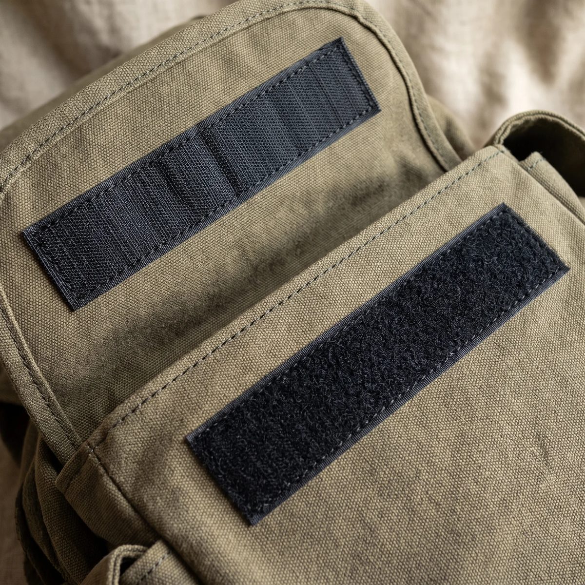 Dos tiras de velcro negro cosidas en la solapa de un morral de lona, con la costura en cuadro visible