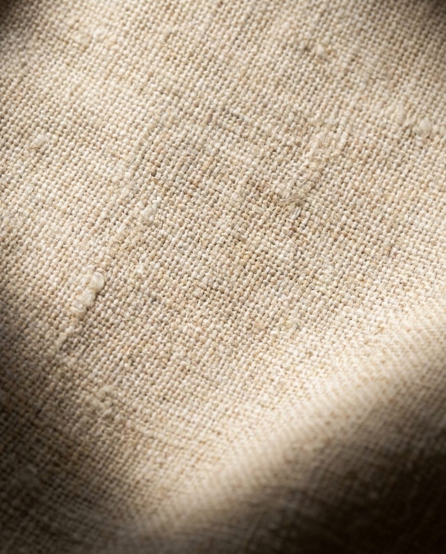 Detalle macro de tela de lino natural mostrando trama y urdimbre, color crudo cálido.